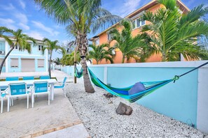 Un hotel frente a la playa con terraza al aire libre, palmeras y una hamaca.
