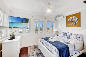 Un dormitorio con cama, televisor, cuadro y ventana con vista a la playa.