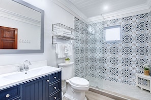 Un baño con lavabo blanco, tocador azul oscuro, inodoro blanco y zona de ducha con azulejos estampados.