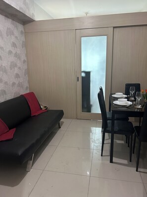 A dining area with a table set for two, a black sofa with red cushions, and a sliding glass door leading outside. - Family Condo SMB2- Live, Love & Laugh at Sea Residences MOA (Pasay City)
