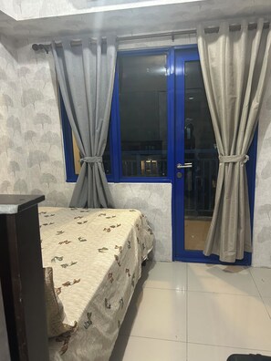 Una habitación con cama, ventana con cortinas, puerta y vista al exterior.