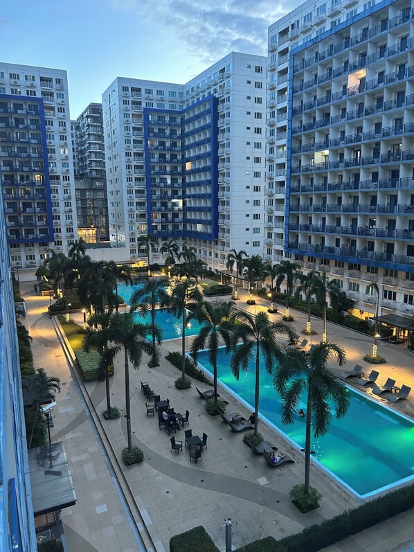Ein Hochhaus-Hotel mit mehreren Balkonen, einem von Palmen umgebenen Swimmingpool und Außenbereich-Sitzgelegenheiten.