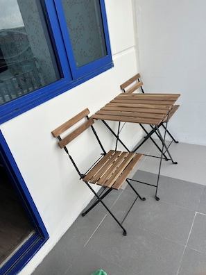 Eine Ecke mit zwei Holztischen und Stühlen, einem Fenster mit blauem Rahmen und einer weißen Wand.