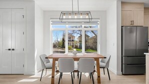 Eine moderne Küche mit einem großen Fenster, einem Esstisch mit Stühlen und einem Kühlschrank.