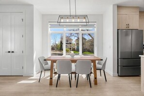 Eine moderne Küche mit einem großen Fenster, einem Esstisch mit Stühlen und einem Kühlschrank.