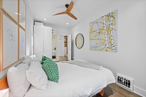 A bedroom with a bed, a ceiling fan, a wall with a painting, and a door leading to another room. - 2 Bed | Central | Min to Saddledome (Calgary)