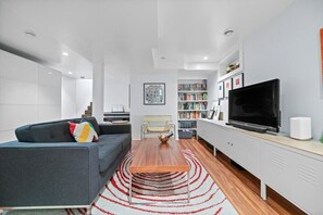 A modern living room with a sofa, coffee table, bookshelf, and a TV. - 2 Bed | Central | Min to Saddledome (Calgary)