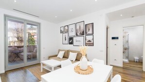 Ein modernes Wohnzimmer mit einem weißen Sofa, einem Esstisch mit einer Vase und einer Glastür, die auf eine Terrasse führt.
