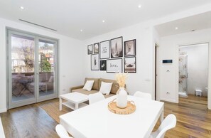 A modern living room with a white sofa, a dining table with a vase, and a glass door leading to a patio. - Design apartment 10 min from downtown with balcony (Torino)