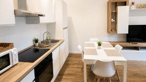 Eine moderne Küche mit weißen Schränken, einer schwarzen Kochplatte und einem Essbereich mit weißem Tisch und Stühlen.