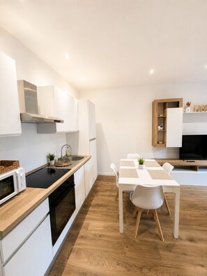 A modern kitchen with white cabinetry, a black stovetop, and a dining area with a white table and chairs. - Design apartment 10 min from downtown with balcony (Torino)