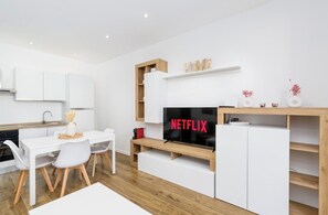 A modern kitchen with white cabinetry, a dining area with a white table and chairs, and a built-in TV with 'NETFLIX' on the screen. - Design apartment 10 min from downtown with balcony (Torino)