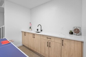 A modern kitchen with a white countertop, wooden cabinets, a black faucet, a small potted plant, and a clock.