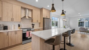 Uma cozinha moderna com armários de madeira, uma ilha central, banquetas e iluminação pendente.