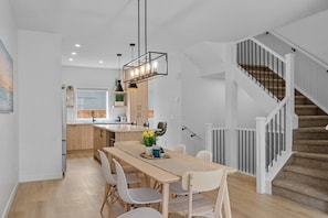 A modern kitchen with a central island, white cabinetry, and a staircase with a railing.
