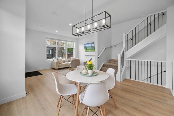 A modern dining area with a round table, white chairs, and a hanging light fixture.