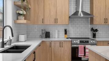 Une cuisine moderne avec des meubles en bois, une hotte en acier inoxydable, un four encastré et une fenêtre offrant une belle vue.