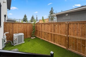 A backyard with artificial grass, a wooden fence, and an air conditioning unit.