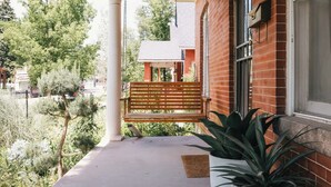 Un porche avec un banc en bois, une plante en pot et un bâtiment en briques en arrière-plan.