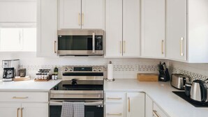 A modern kitchen with white cabinets, a stainless steel microwave, an oven, and a coffee maker. - Denver Basecamp | Workspace | Pet-Friendly 30+ (Denver)