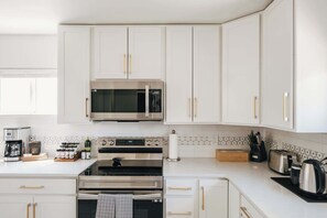 Eine moderne Küche mit weißen Schränken, einer Edelstahl-Mikrowelle, einem Backofen und einer Kaffeemaschine.