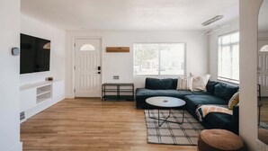 A living room with a dark green sofa, a round coffee table, a patterned rug, a TV mounted on the wall, and a door with a window. - Denver Basecamp | Workspace | Pet-Friendly 30+ (Denver)