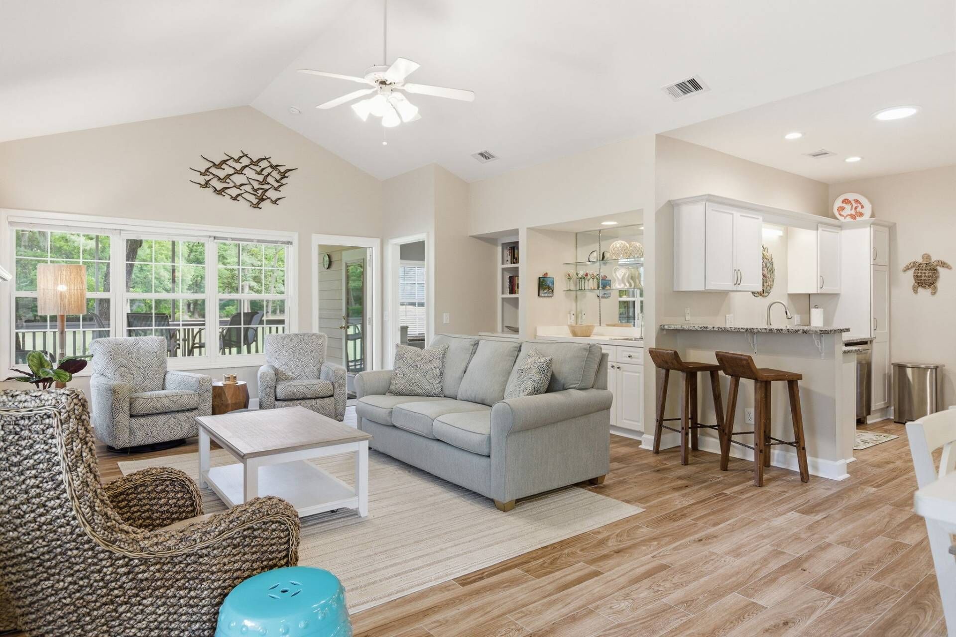 A spacious living area with a sofa, chairs, a coffee table, a kitchen with bar stools, and a ceiling fan.