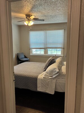 A bedroom with a bed, a chair, a ceiling fan, and a window with blinds. - Central 2BR Home with AC: Near Texas Tech & Covenant Medical Center (Lubbock)