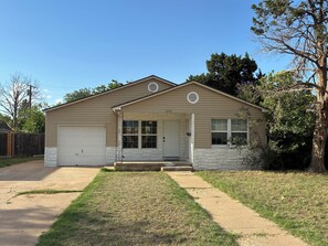 A single-story house with a garage, a front porch, and a small front yard. - Central 2BR Home with AC: Near Texas Tech & Covenant Medical Center (Lubbock)