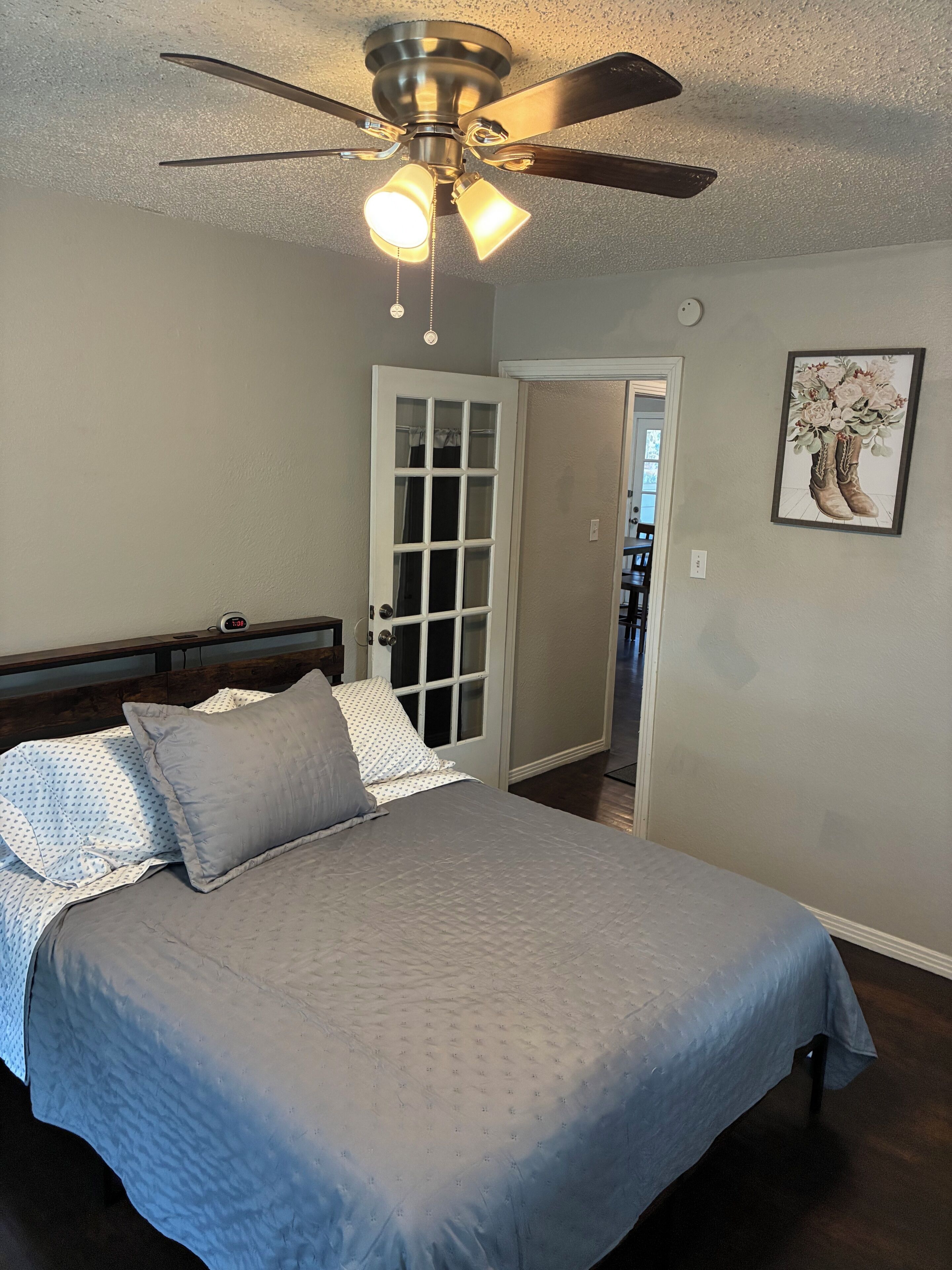 A bedroom with a bed, a ceiling fan, a door, and a framed picture on the wall.