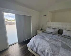 Ein Schlafzimmer mit Bett, Nachttisch, Fenster mit Vorhängen und Blick ins Freie.
