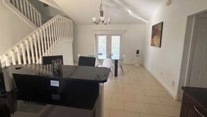 A dining area with a glass table and chairs, a staircase with white railings, a chandelier, and a door on the right. - Spacious 4-bedroom house in delightful Cape Coral with AC (Cape Coral)
