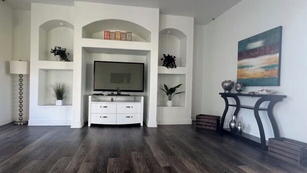 A living room with a flat-screen TV, white shelving, a console table, and a painting on the wall. - Spacious 4-bedroom house in delightful Cape Coral with AC (Cape Coral)