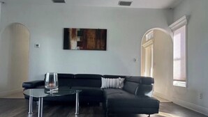 A modern living room with a sectional sofa, a glass coffee table, and a large abstract painting on the wall. - Spacious 4-bedroom house in delightful Cape Coral with AC (Cape Coral)