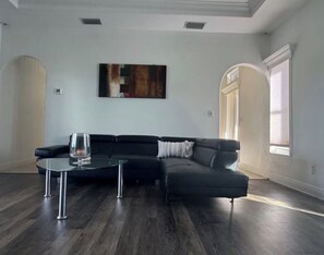 Ein modernes Wohnzimmer mit einer Eckcouch, einem Glastisch und einem großen abstrakten Gemälde an der Wand.