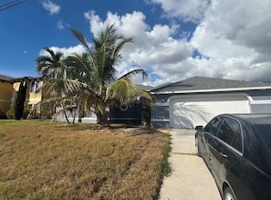 A residential area with a house, a garage, and a parked car. - Spacious 4-bedroom house in delightful Cape Coral with AC (Cape Coral)