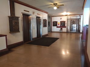 A hallway with three elevators, a wooden cabinet, a black doormat, and a ceiling fan.