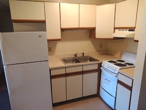 A compact kitchen with a refrigerator, double sink, stove, and wooden cabinets.
