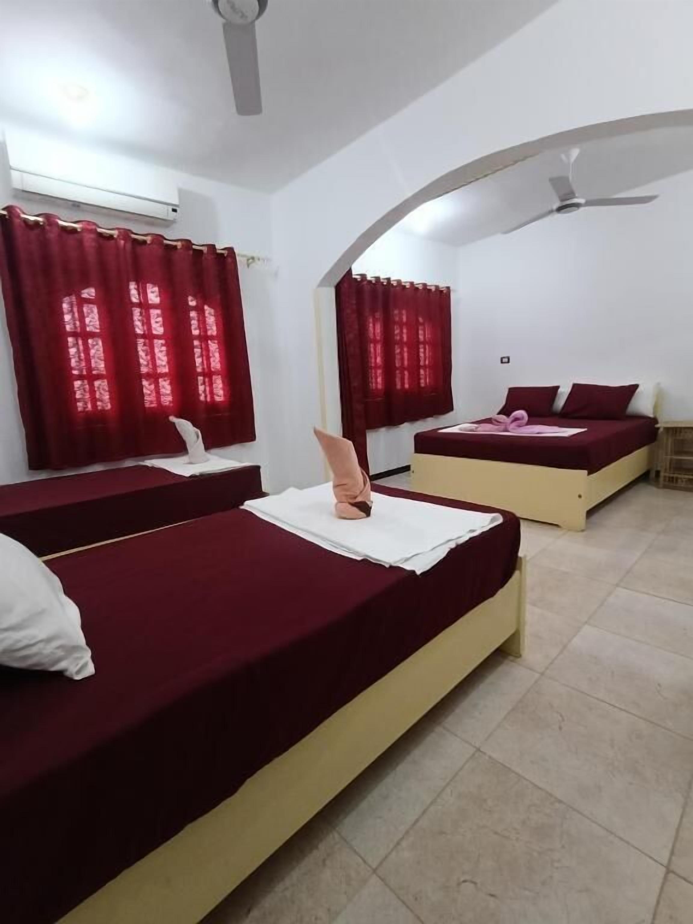 A room with two beds, red curtains, a ceiling fan, and an air conditioning unit.