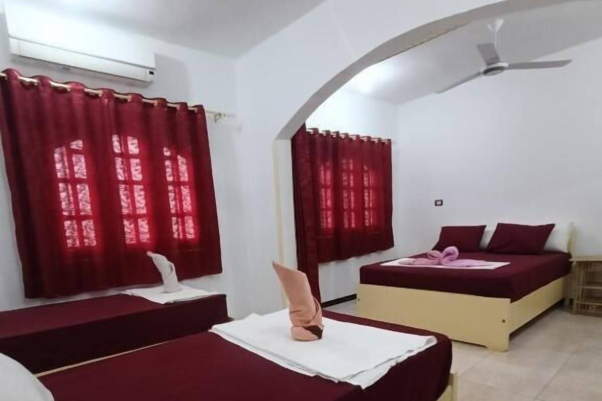 A room with two beds, red curtains, a ceiling fan, and an air conditioning unit.