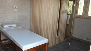 Ein Zimmer mit Holzschrank, Bett mit weißer Matratze und Fenster mit Blick ins Grüne.