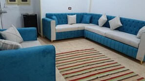 A living room with a blue sectional sofa, a small table, and a striped rug. - ABU Guest House (Aswan)
