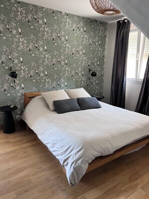 Ett sovrum med en säng, två sängbord, en vägglampa och ett fönster med gardiner.