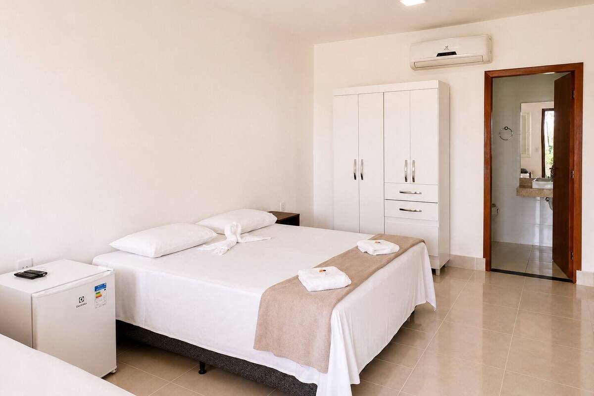 Una habitación de hotel con cama, mesita de noche, armario y equipo de aire acondicionado.