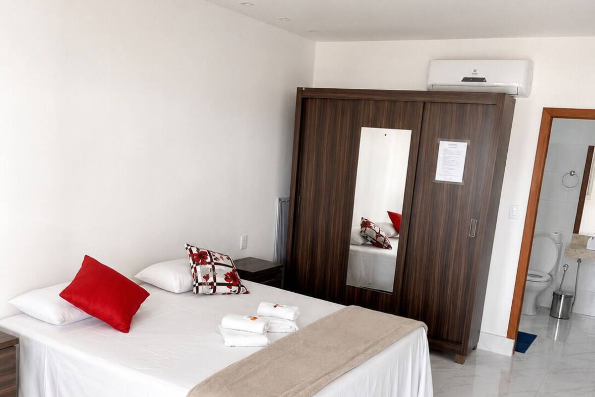 Habitación de hotel con cama, armario, espejo y baño visible a través de una puerta abierta.