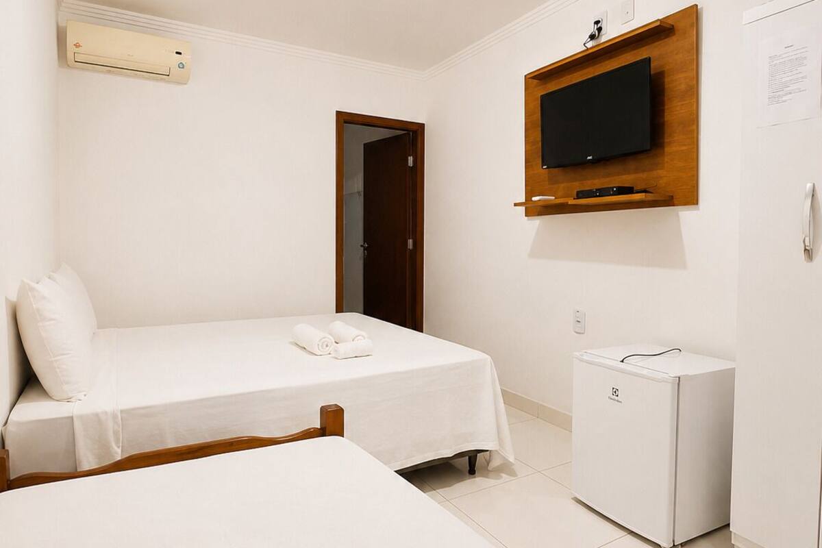 Habitación de hotel con cama, mesita de noche, televisor montado en la pared y refrigerador.