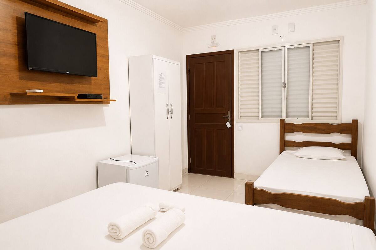 Un dormitorio con cama, armario, televisor y ventana con contraventanas.