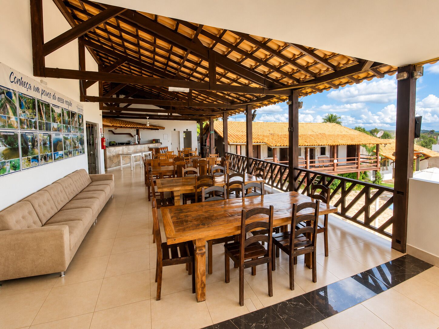 Un área de comedor cubierta con mesas y sillas de madera, un sofá y vistas del paisaje circundante.