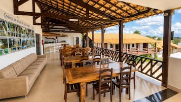 Un área de comedor cubierta con mesas y sillas de madera, un sofá y vistas del paisaje circundante.