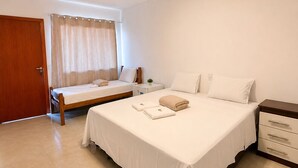Quarto com uma cama grande, uma cama menor, uma mesa de cabeceira, um guarda-roupa de madeira e uma porta.